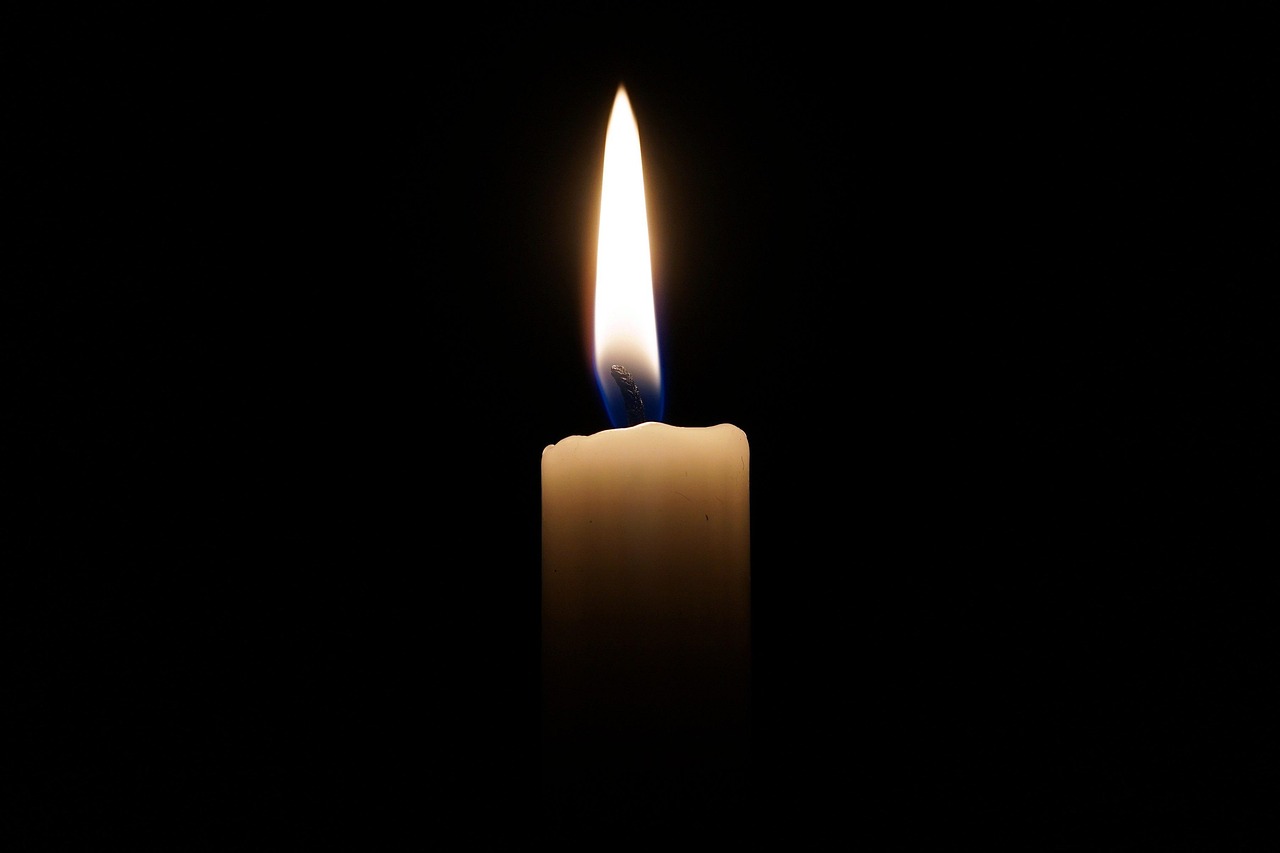 A candle wick trimmer next to a soy candle on a wooden shelf