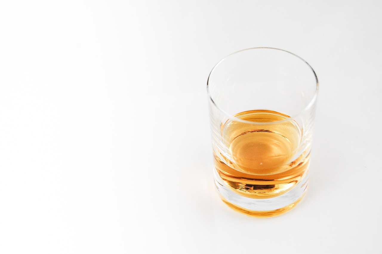Hand blown whiskey tumbler sitting on a bar shelf with a bottle of whiskey