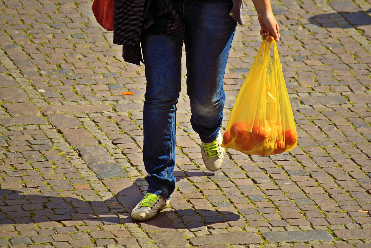 A heavy reusable shopping bag loaded with produce and groceries held by a person