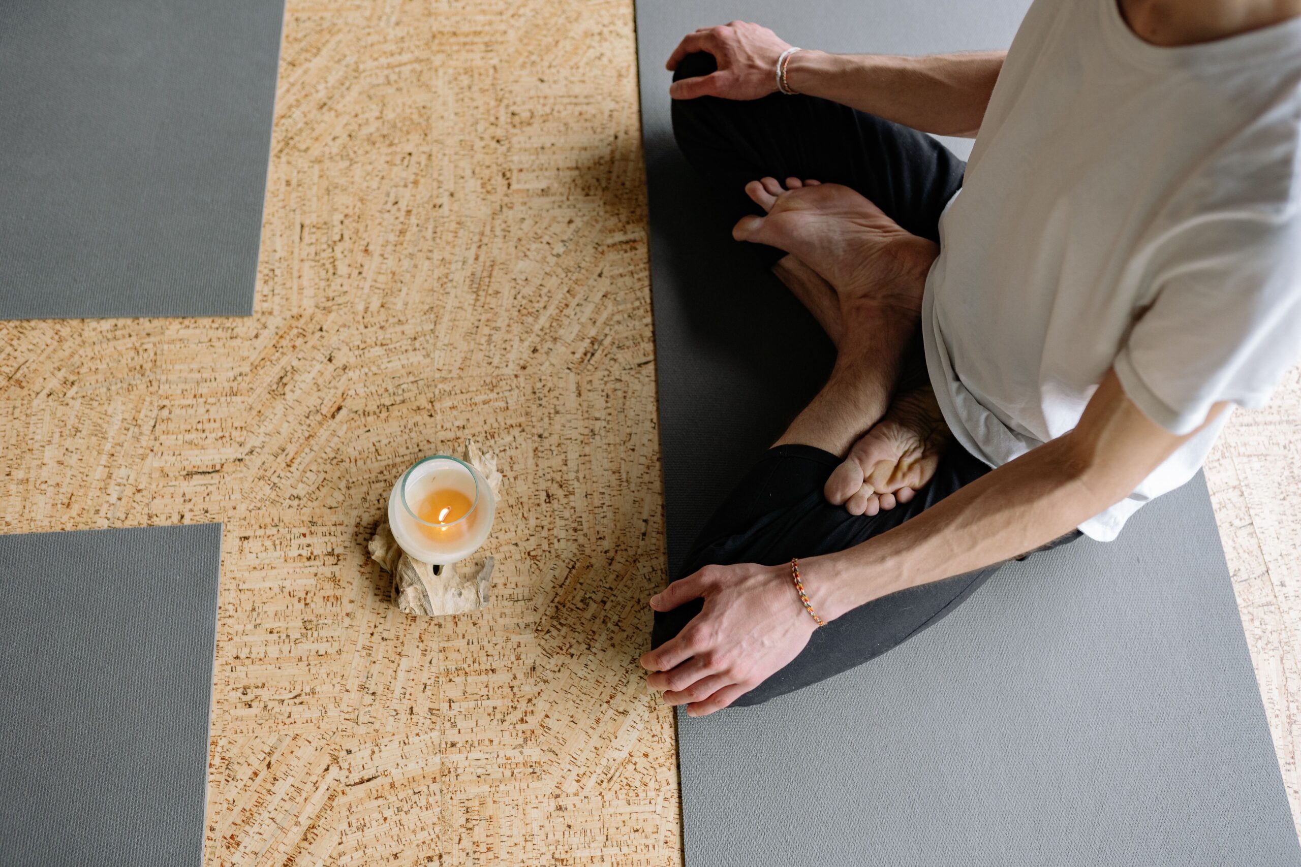 Adult meditating in lotus pose on yoga mat with candle, creating a calming atmosphere.