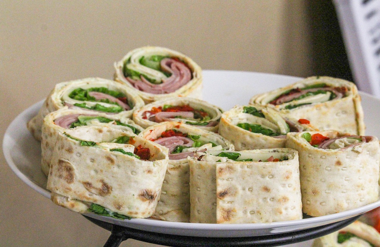 A reusable sandwich wrap made of fabric with a snap closure, placed on a wooden cutting board next to fresh bread and lettuce leaves
