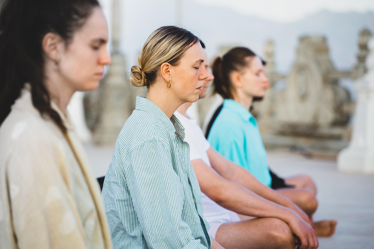 A group of people practicing yoga outdoors on a wooden platform in a forest setting during a retreat