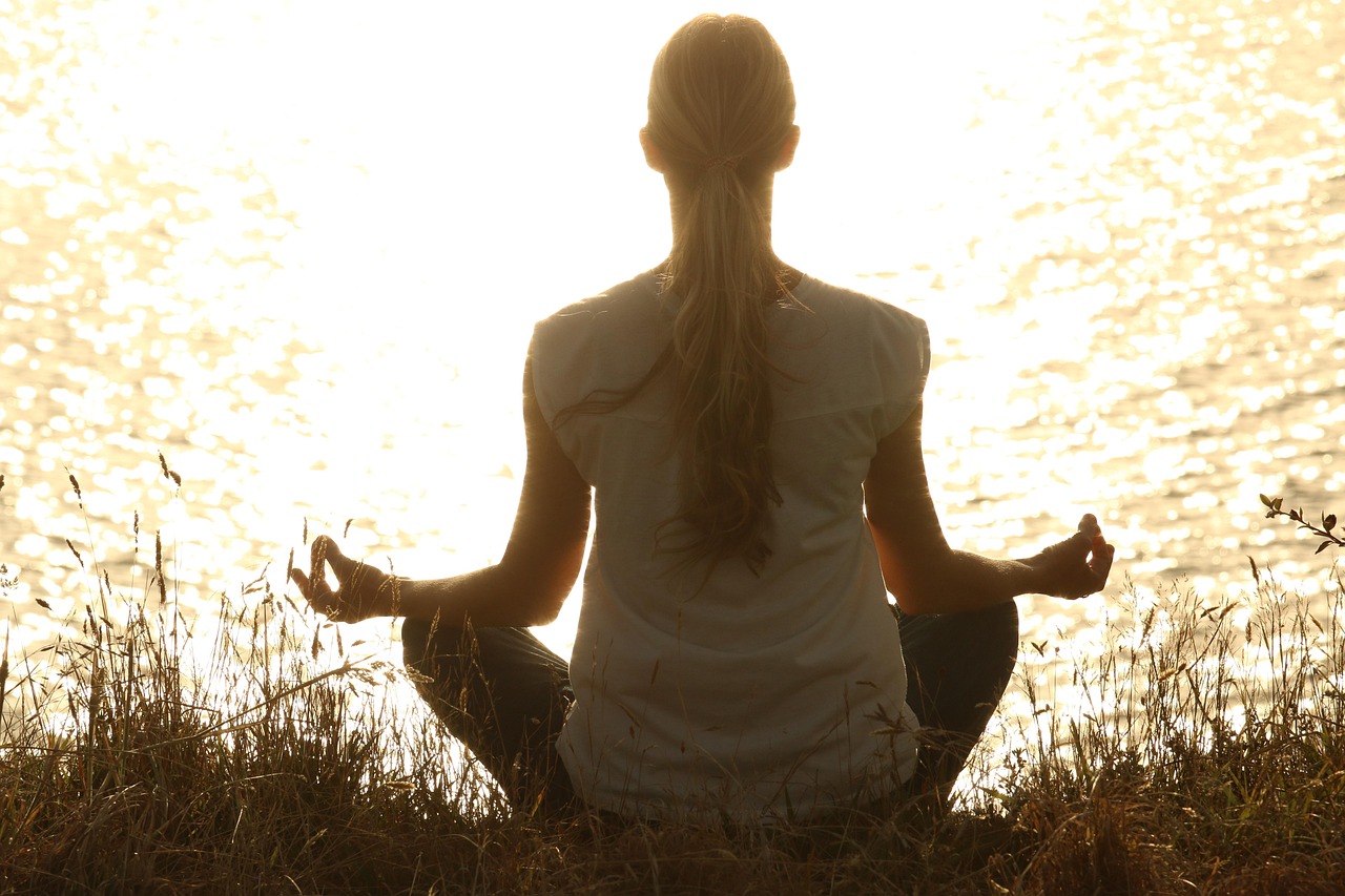 A woman meditating in a peaceful yoga pose on a cliff during a tropical sunset at a yoga retreat